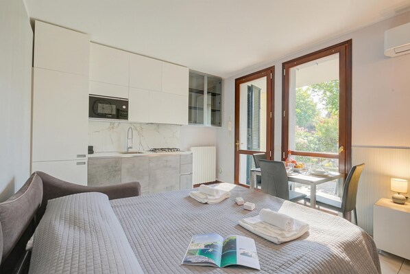 Une chambre d’hôtel moderne équipée d’un lit, d’une petite table à manger, d’un coin cuisine et de grandes fenêtres.