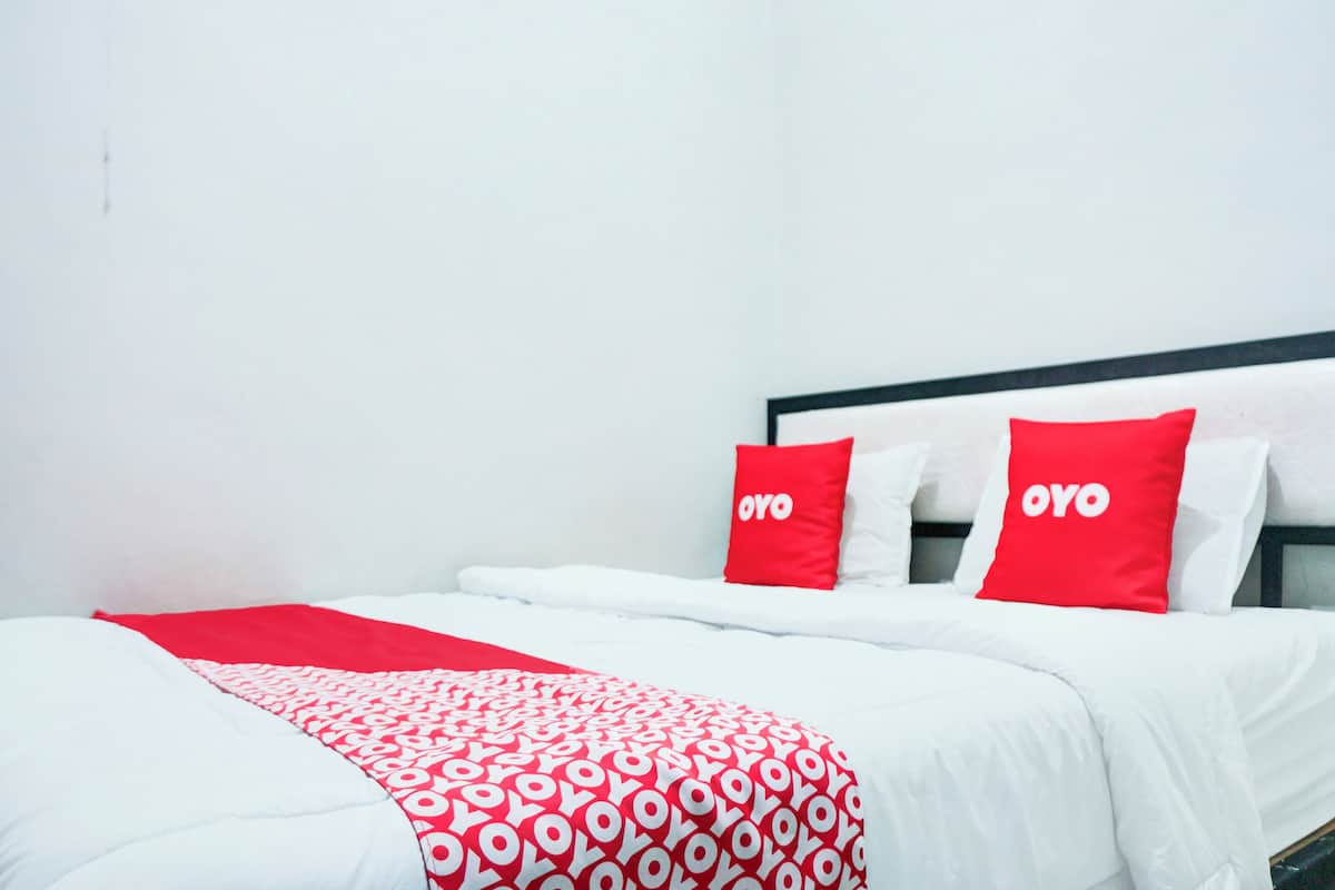 A hotel room with a bed featuring red and white bedding, two pillows with the word "OYO" on them, and a red and white patterned throw blanket.