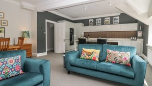 Ein modernes Wohnzimmer mit türkisfarbenen Sofas, einem Essbereich und einer Küche mit weißen Schränken und einer Holz Arbeitsplatte.