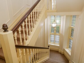 A grand staircase with a wooden handrail and white balusters, leading to a landing with a large window with decorative glass panes. - Lake House Loft (Windermere)