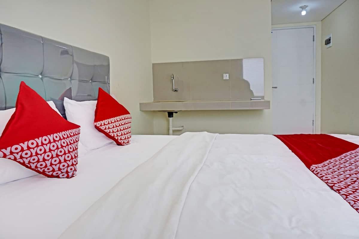 A hotel room with a bed, red and white pillows, a headboard, a mirror, a sink, and a door.