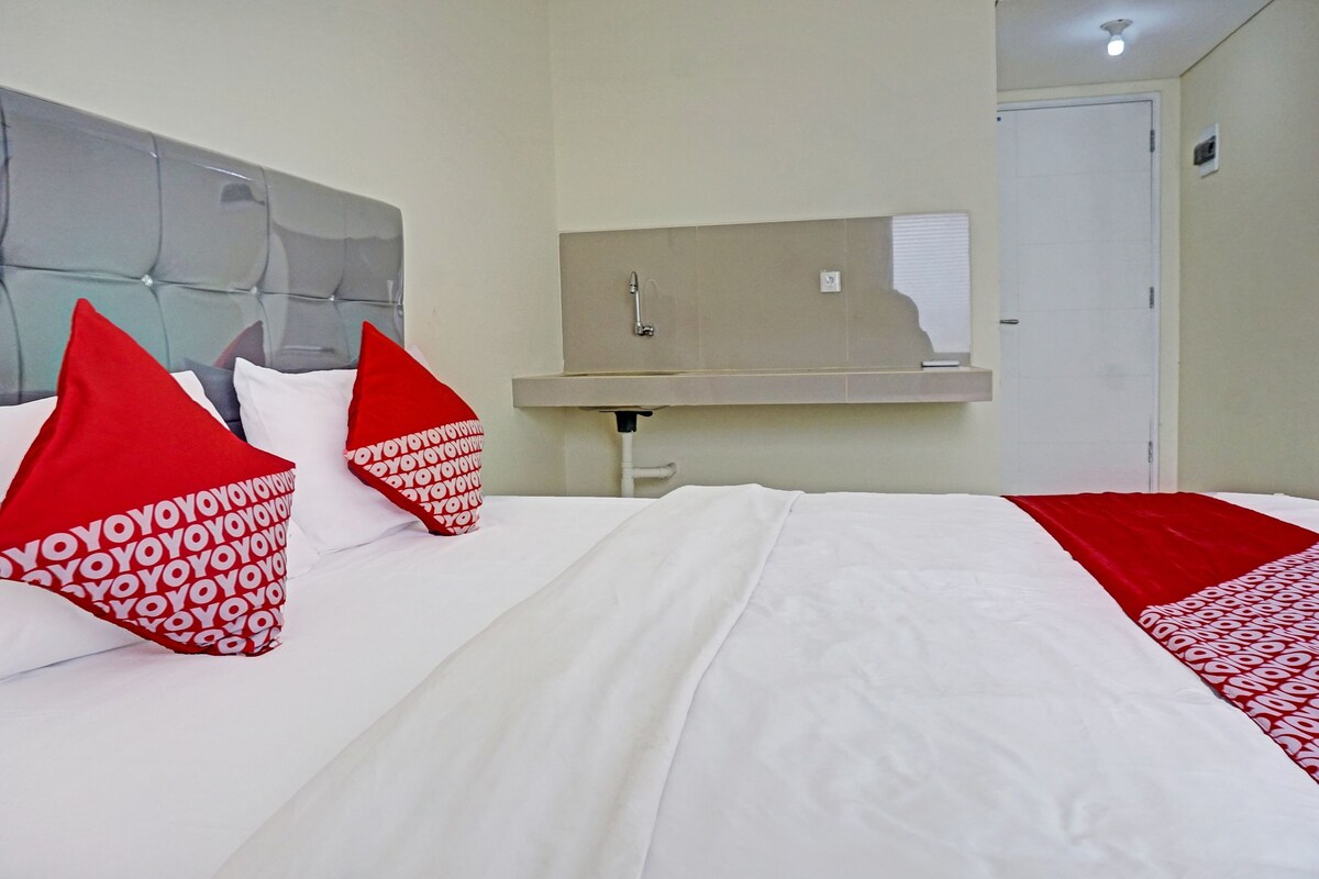 Une chambre d’hôtel avec un lit, des oreillers rouges et blancs, une tête de lit, un miroir, un lavabo et une porte.