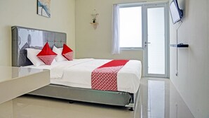 A bedroom with a bed, a bedside table, a wall-mounted TV, a window with blinds, and an air conditioning unit. - Hotel O Skyland Bogorienze Apartment (Bogor)
