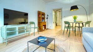 Ein modernes Wohnzimmer mit Flachbildfernseher, Bücherregal, Essbereich mit Stühlen und einer Lampe.