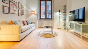 Ein Wohnzimmer mit einer Couch, einem Couchtisch, einem Fernseher, einem Bücherregal und einem Fenster mit Blick.