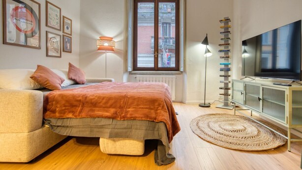 Ein Schlafzimmer mit einem Bett, einem Fernseher, einer Heizung, einem Fenster und einer Lampe.