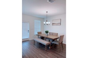A dining room with a wooden table, benches, and chairs. There is a chandelier above the table and a window with blinds.