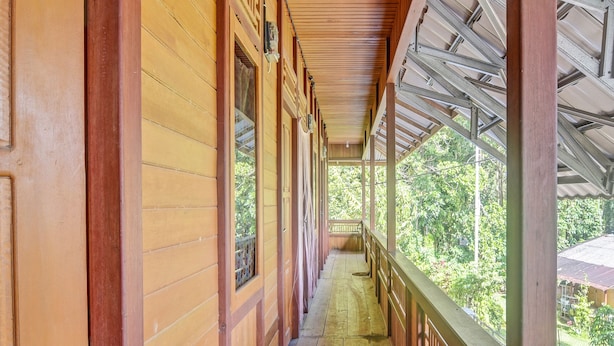 A covered corridor with wooden walls and a metal roof, leading to a balcony with a view of greenery. - Hotel O Sosonopan Homestay Near LANTAMAL VIII MANADO (Manado)