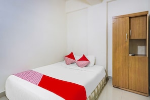 A neatly made bed with a white and red bedspread, two red pillows, and a wooden wardrobe in a simple room.