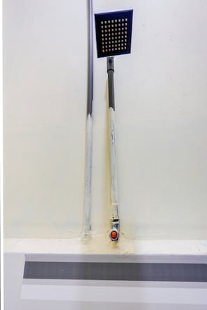 A showerhead mounted on a wall with a visible pipe and a control valve.