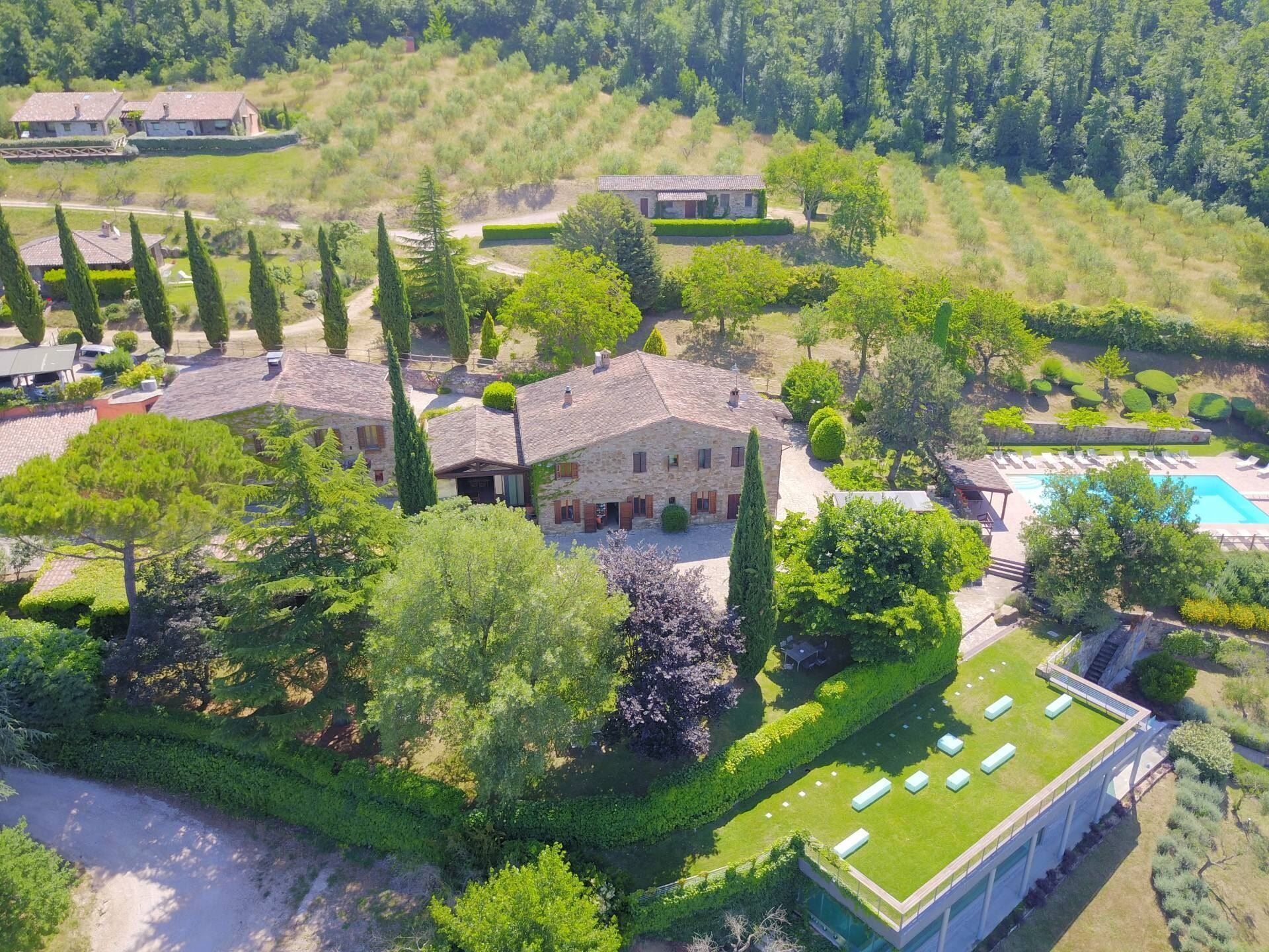 Une vue aérienne d’un vaste domaine, avec un bâtiment central en pierre entouré de jardins bien entretenus, d’une piscine et d’un espace extérieur aménagé avec des sièges.