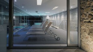 Area piscina interna moderna con sedie a sdraio e parete in vetro.