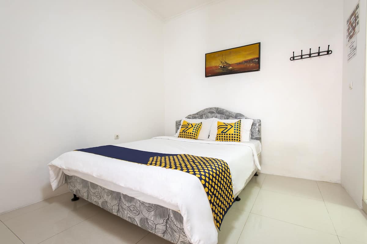 A single-bed room with a white and gray patterned bedspread, a blue and yellow blanket, and a painting on the wall.