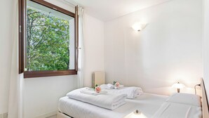 A bedroom with a bed, a window with curtains, a bedside lamp, and a view of trees outside. - Porto Letizia Venezia 8, Porlezza, Italy (Porlezza)