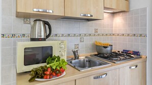 A kitchen with wooden cabinets, a microwave, a kettle, a sink, and a gas stove. - Porto Letizia Venezia 8, Porlezza, Italy (Porlezza)