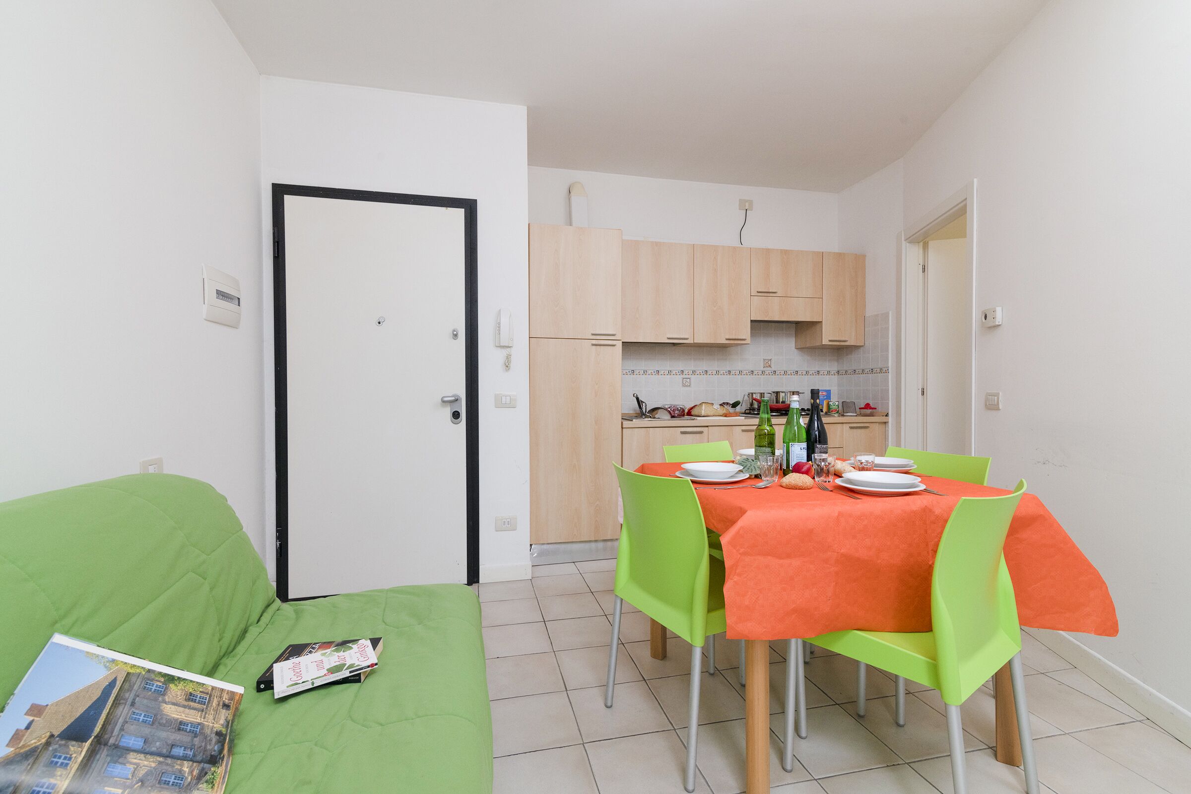 A compact living space with a dining area, kitchenette, and a green sofa with a magazine.