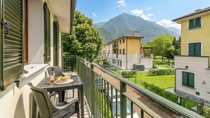 A balcony with a table, a bottle, and a plate of food. In the background, there are buildings and a mountain. - Porto Letizia Roma 5, Porlezza, Italy (Porlezza)