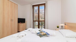 A hotel room with a bed, a TV, a window with a view, and a wooden wardrobe. - Porto Letizia Napoli 7, Porlezza, Italy (Porlezza)