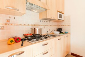 A kitchen with wooden cabinets, a gas stove, a microwave, and a tiled backsplash. - Porto Letizia Napoli 7, Porlezza, Italy (Porlezza)