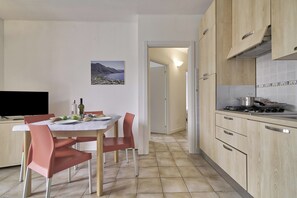 A kitchen with a dining table, chairs, and a TV. There is a painting on the wall and a door leading to another room. - Porto Letizia Firenze 4, Porlezza, Italy (Porlezza)