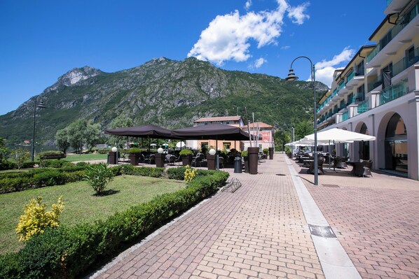 A paved walkway with outdoor seating, a mountain backdrop, and a building with balconies. - Porto Letizia Firenze 2, Porlezza, Italy (Porlezza)