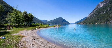 A clear lake with mountains in the background, a sandy beach, and people swimming.