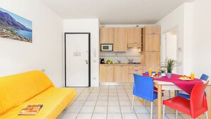 A compact living space with a kitchenette, a dining area with a table and chairs, a sofa, and a door with a keypad lock.