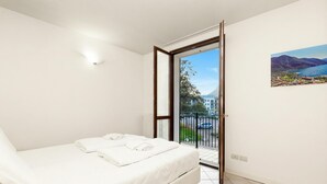 A bedroom with a bed, a painting, a window, and a door leading to a balcony.