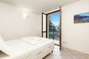 Une chambre à coucher avec un lit, un tableau, une fenêtre et une porte donnant sur un balcon.