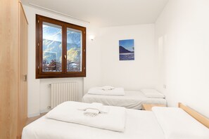 A bedroom with two beds, a wooden wardrobe, a radiator, and a window with a mountain view.