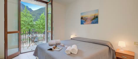 Een slaapkamer met een bed, nachtkastje, schilderij en balkon met stoelen en een tafel.