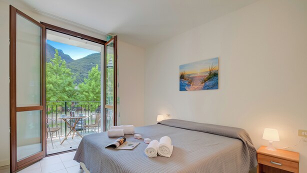 A bedroom with a bed, a nightstand, a painting, and a balcony with chairs and a table. - Porto Letizia Firenze 1, Porlezza, Italy (Porlezza)