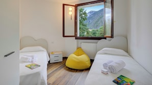 A bedroom with two beds, a yellow bean bag, a nightstand, and a view of a mountainous landscape. - Porto Letizia Firenze 1, Porlezza, Italy (Porlezza)