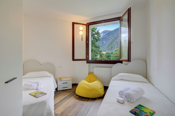 A bedroom with two beds, a yellow bean bag, a nightstand, and a view of a mountainous landscape.