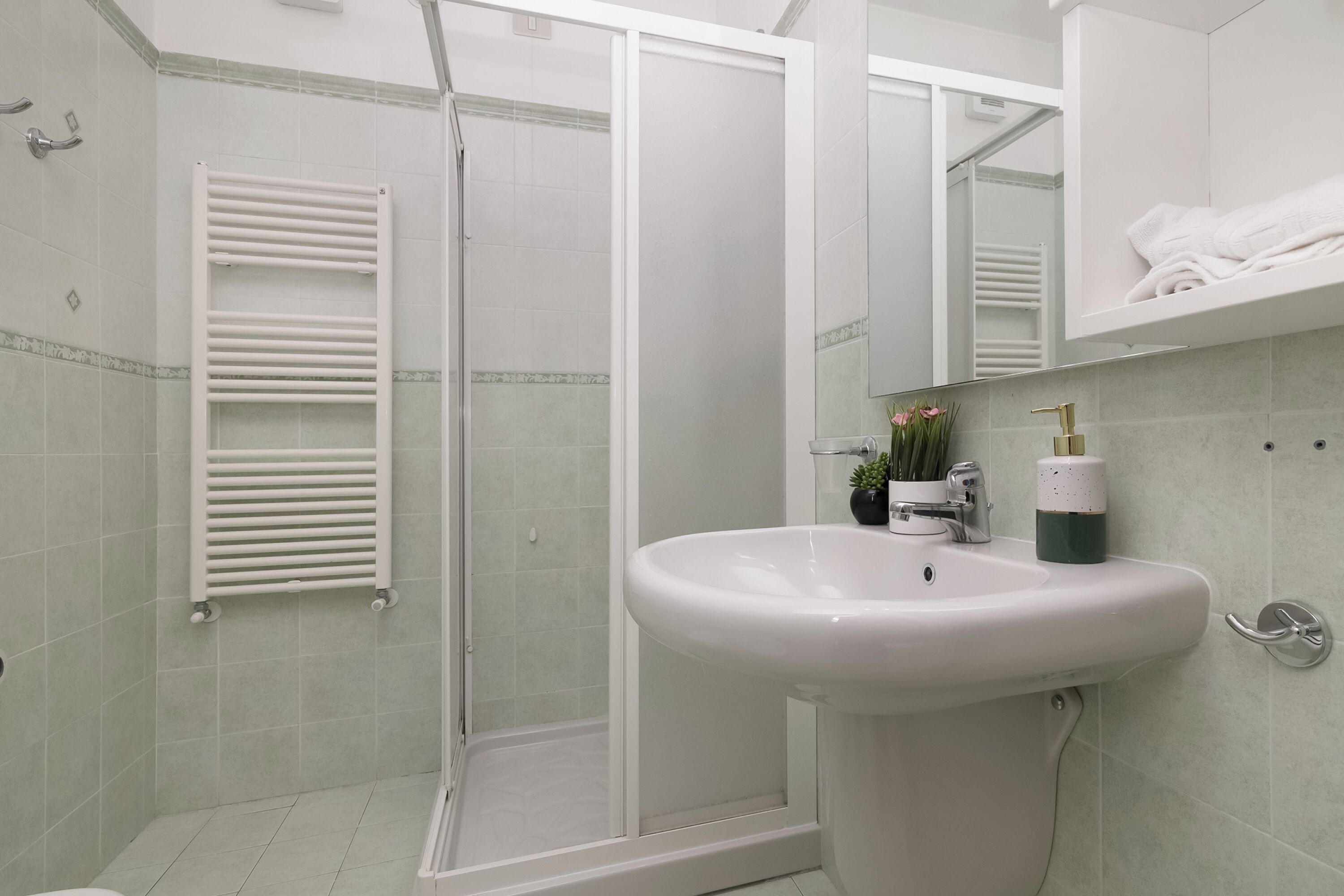 A bathroom with a shower, a sink, and a towel rack.