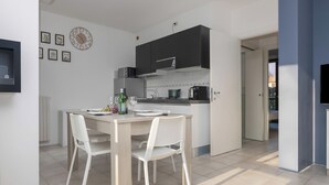 Moderni keittiö, jossa on ruokapöytä ja -tuolit, seinällä oleva kello ja näkymä viereiseen huoneeseen.