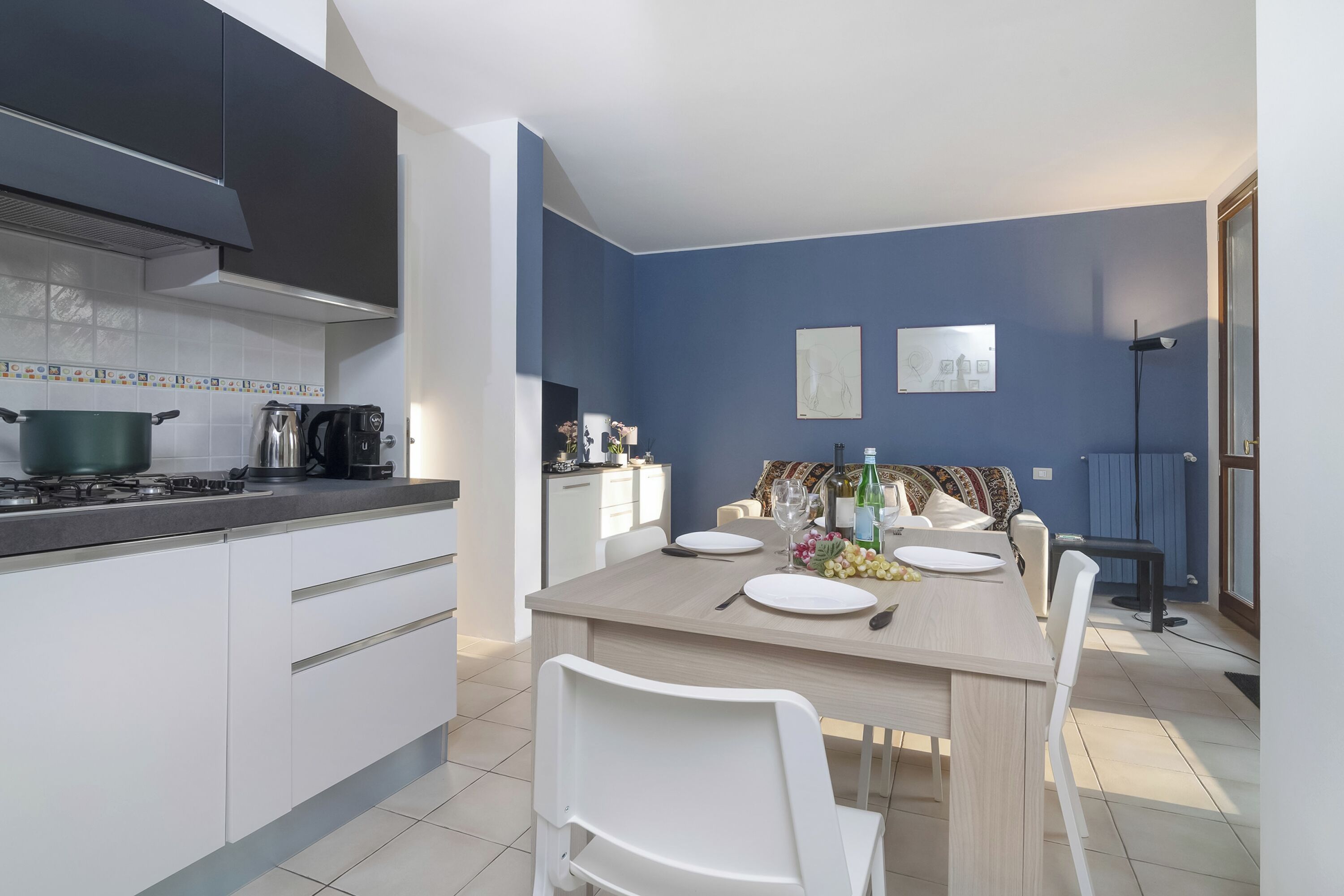 A modern kitchen with white cabinets, a wooden dining table set for four, and a blue accent wall.