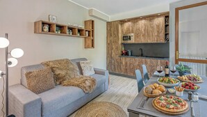 En moderne stue med en grå sofa, træhylder og et spiseområde med pizza og salat.