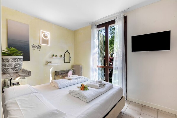 A hotel room with a bed, a TV, a bathroom, and a window with curtains. - Porto Letizia Venezia 2, Porlezza, Italy (Porlezza)