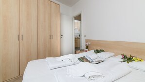 A hotel room with a large wooden wardrobe, a neatly made bed with white linens, a small bedside table with a book and a vase of flowers. - Porto Letizia Tchaikovsky 3, Porlezza, Italy (Porlezza)