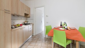 A kitchen with wooden cabinets, a dining table with green chairs, and a white tiled backsplash. - Porto Letizia Tchaikovsky 3, Porlezza, Italy (Porlezza)