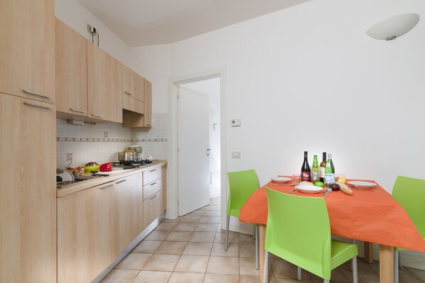 A kitchen with wooden cabinets, a dining table with green chairs, and a white tiled backsplash.