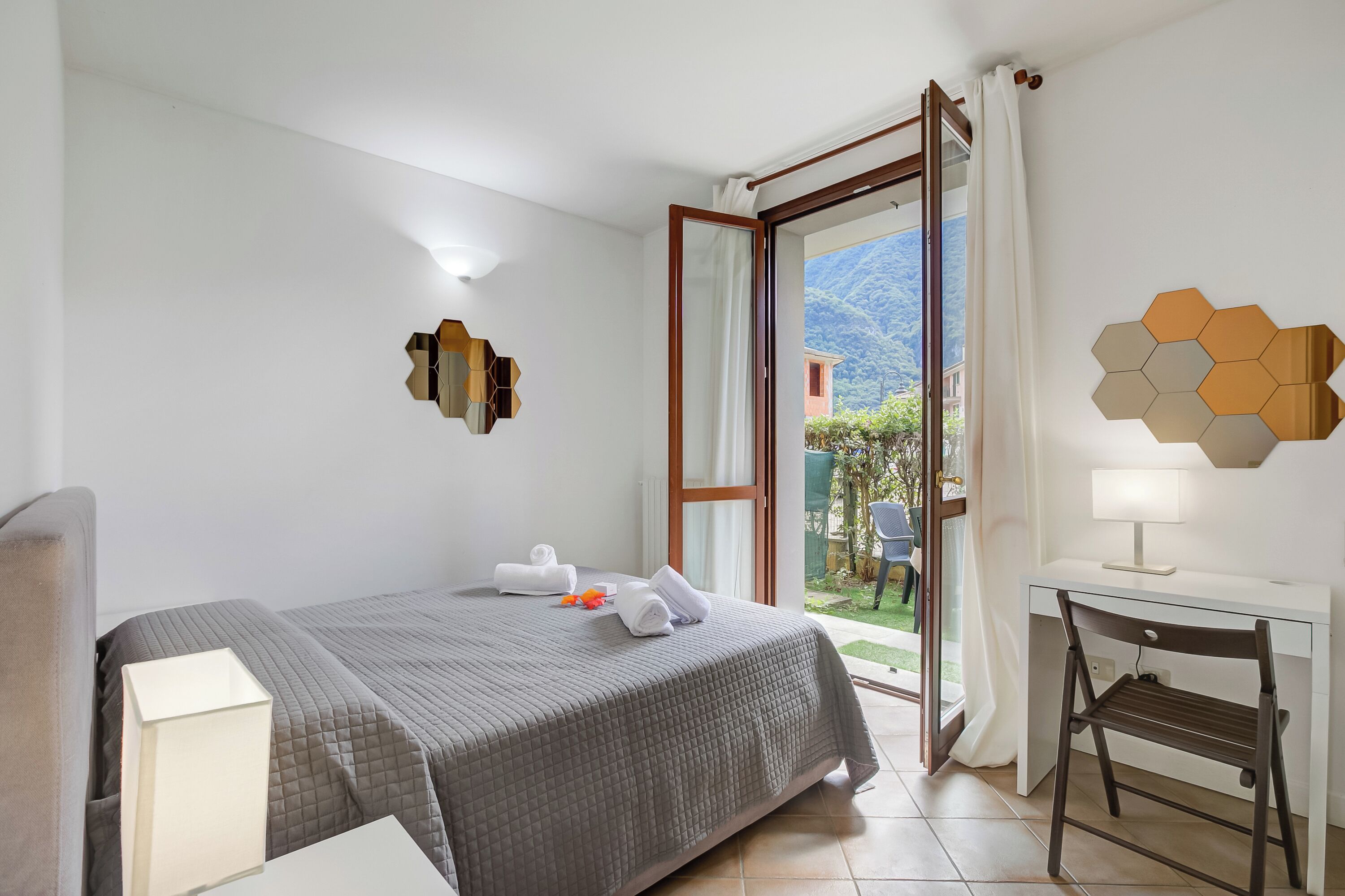A hotel room with a bed, a desk, a chair, and a view of the outdoors.