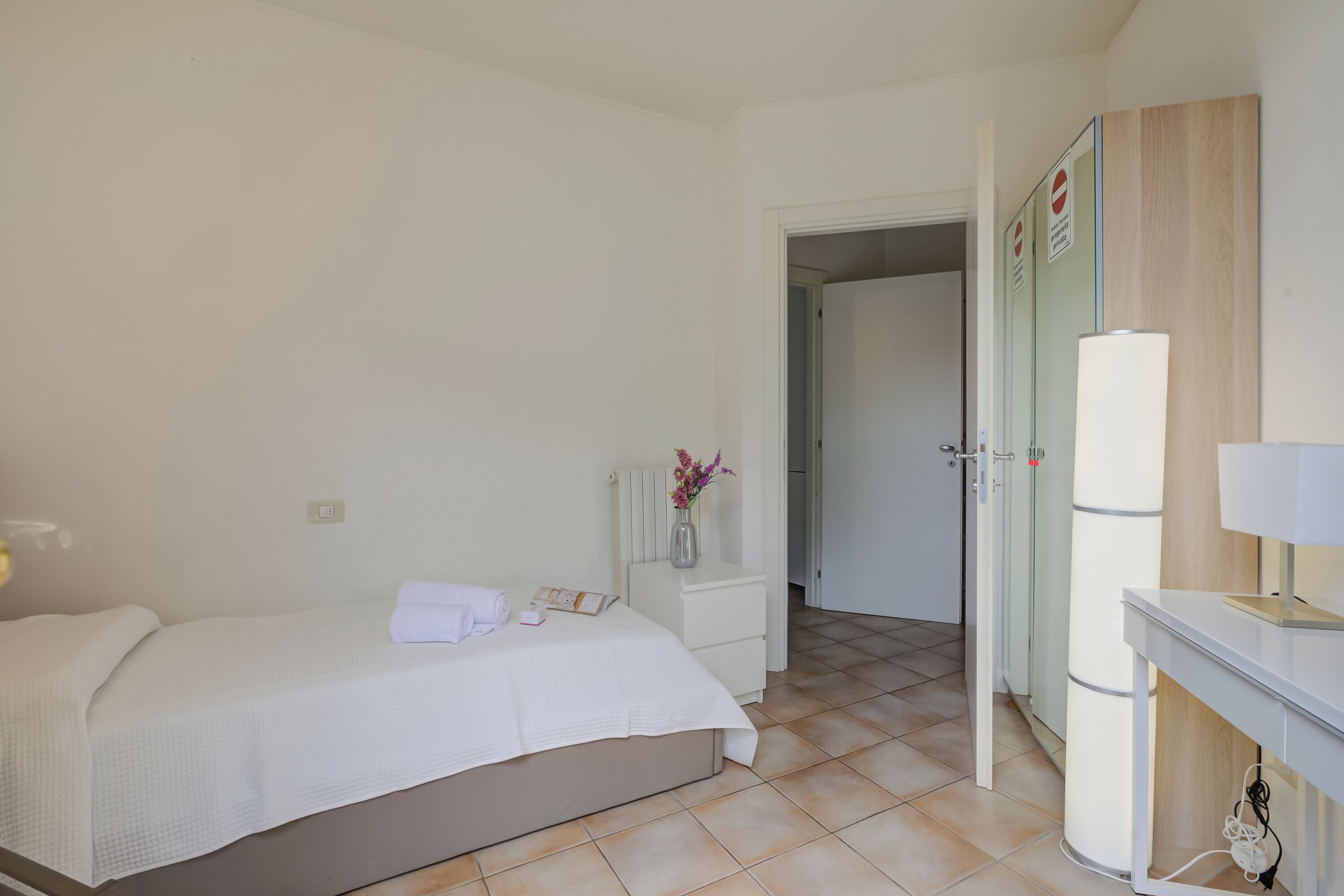A hotel room with a bed, bedside table, lamp, and a door leading to a bathroom.
