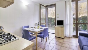 A compact kitchen with a gas stove, a dining table with chairs, a television, and a sofa. - Porto Letizia Como 3, Porlezza, Italy (Porlezza)