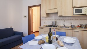 A compact kitchen with wooden cabinets, a microwave, and a dining area with a table set for two. - Porto Letizia Como 3, Porlezza, Italy (Porlezza)