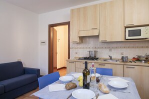 A compact kitchen with wooden cabinets, a microwave, and a dining area with a table set for two.