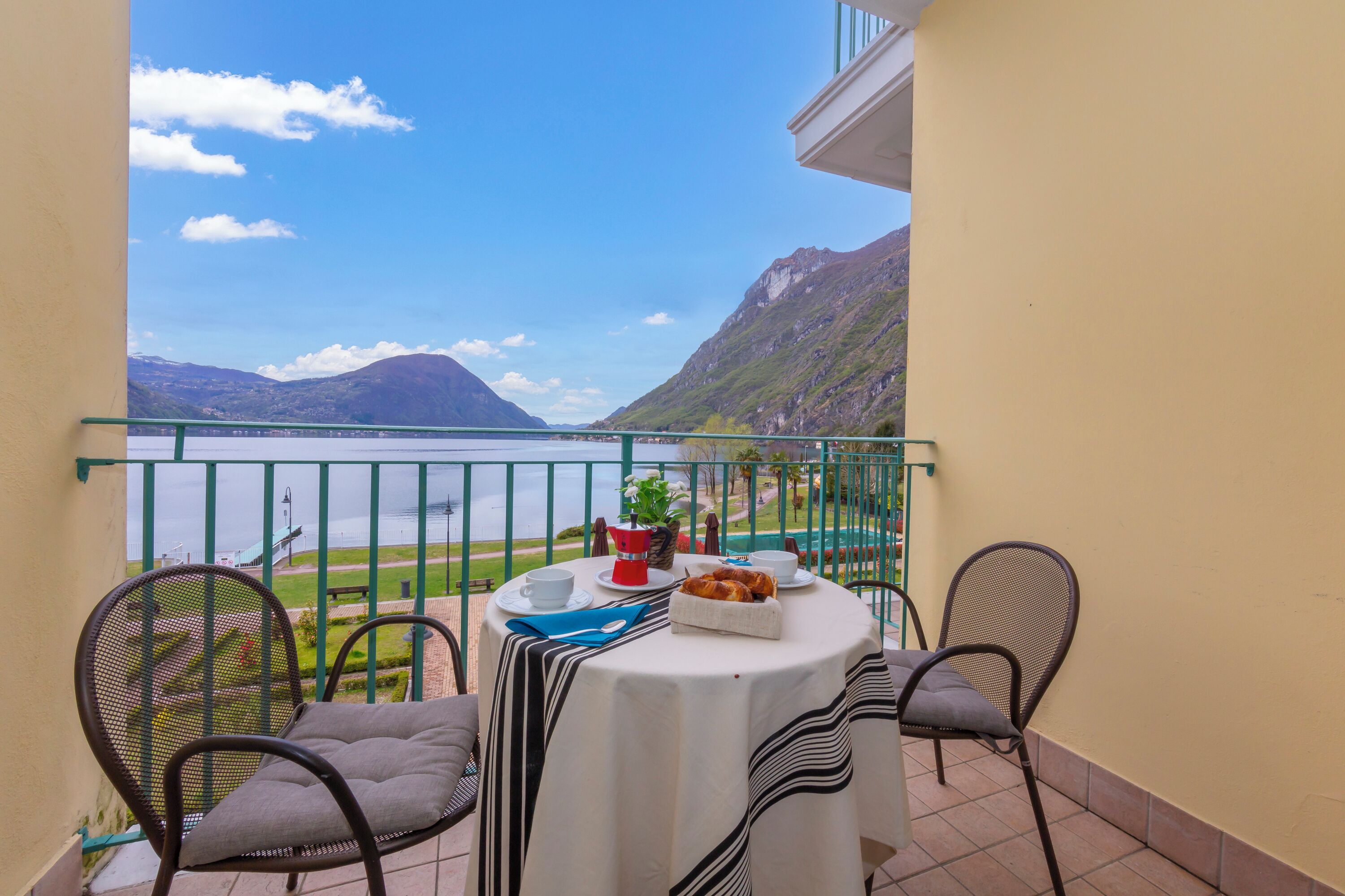 Un balcon avec une table dressée pour deux personnes, offrant une vue sur un lac et des montagnes.