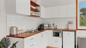 Een moderne keuken met witte kastjes, een roestvrijstalen spoelbak, een waterkoker, een broodrooster en een broodbak.