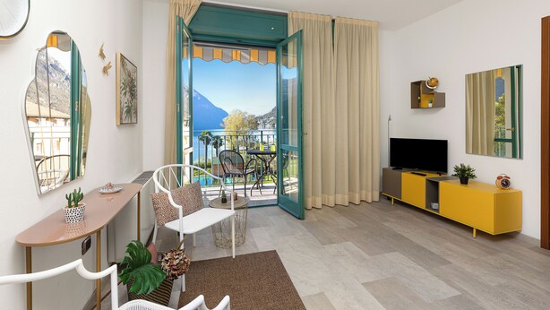 A modern living room with a TV, yellow entertainment unit, and a view of a balcony with outdoor furniture.